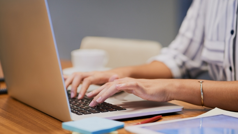 Osoba kuca na laptopu za stolom
