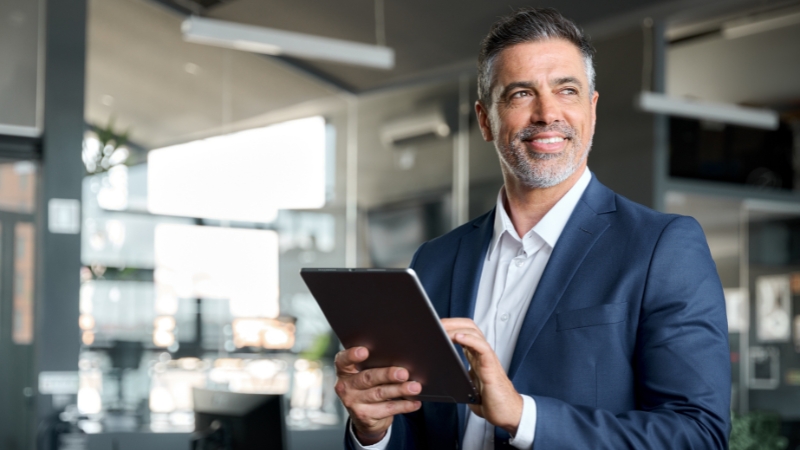 Nasmejan poslovni čovek u odelu drži tablet u modernom kancelarijskom prostoru