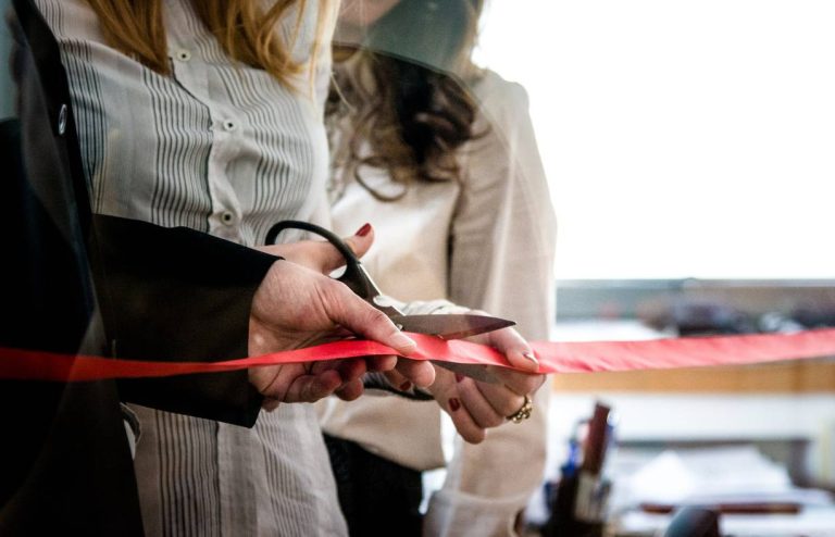 Grupa nasmejanih ljudi svečano seče vrpcu povodom otvaranja novog biznisa.