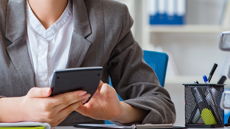 Knjigovođa sedi za stolom u kancelariji i koristi digitron pored radnog pribora