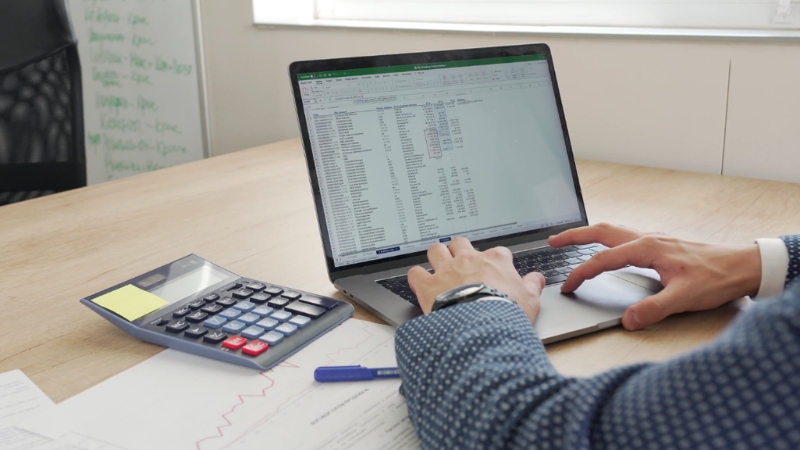 Knjigovođa radi obračun i administraciju na laptopu uz kalkulator i poslovne papire na stolu