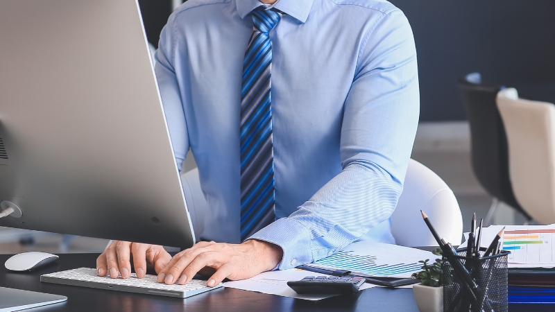 Knjigovođa radi za računarom za radnim stolom sa poslovnim dokumentima