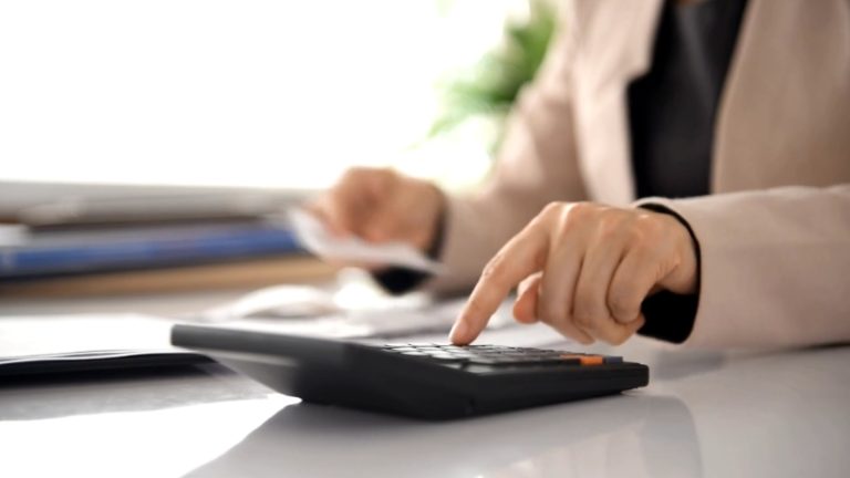 Knjigovođa u kancelariji koristi digitron i pregledа poslovnu dokumentaciju na stolu