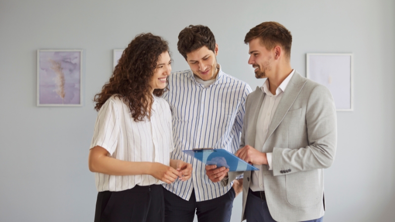 Dvoje zakupaca i agent za nekretnine zajedno pregledaju dokumentaciju u praznom stanu