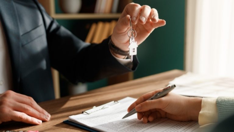 Osoba predaje ključeve stana dok druga potpisuje ugovor o zakupu za stolom u kancelariji