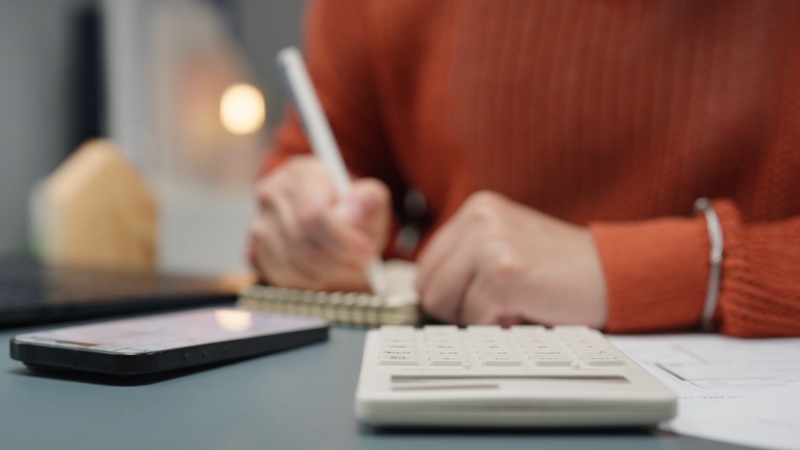 Osoba računa poslovni promet na kalkulatoru i zapisuje iznose kako bi pratila limit za ulazak u PDV sistem