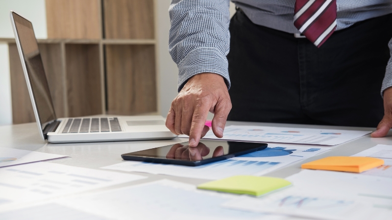 Osoba analizira poslovne podatke na tabletu uz papire i laptop