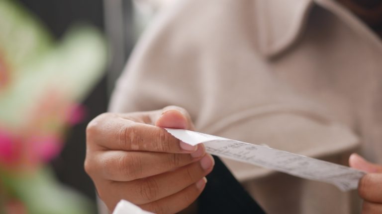 Kupac drži pogrešno otkucan fiskalni račun i pažljivo proverava iznos na papiru