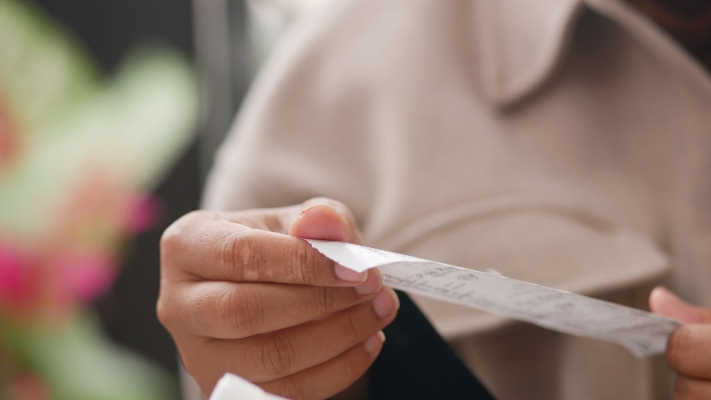 Kupac drži pogrešno otkucan fiskalni račun i pažljivo proverava iznos na papiru