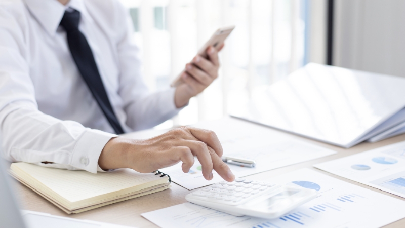 Osoba proverava finansijske izveštaje i računa troškove na kalkulatoru tokom poslovne analize