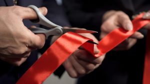 Muškarac svečano seče crvenu traku kao simboličan početak procesa otvaranje preduzetničke radnje