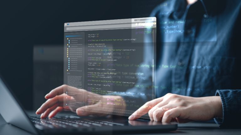 Osoba kuca kod na laptopu dok se na ekranu vidi programski interfejs i linije koda