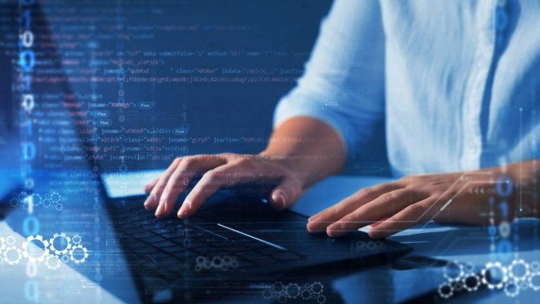 Osoba kuca kod na laptopu, sa digitalnim prikazom programskog jezika i podataka preko ekrana