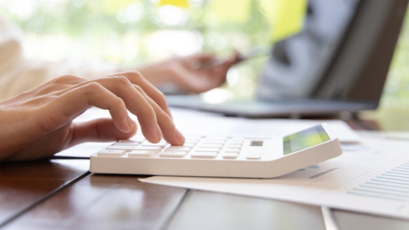 Osoba računa poslovni promet na kalkulatoru pored laptopa i finansijskih dokumenata