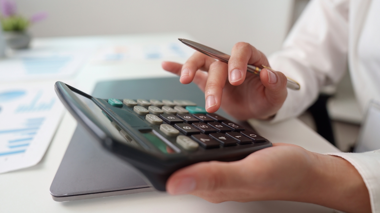 Osoba računa troškove na kalkulatoru uz beleške i grafike na stolu