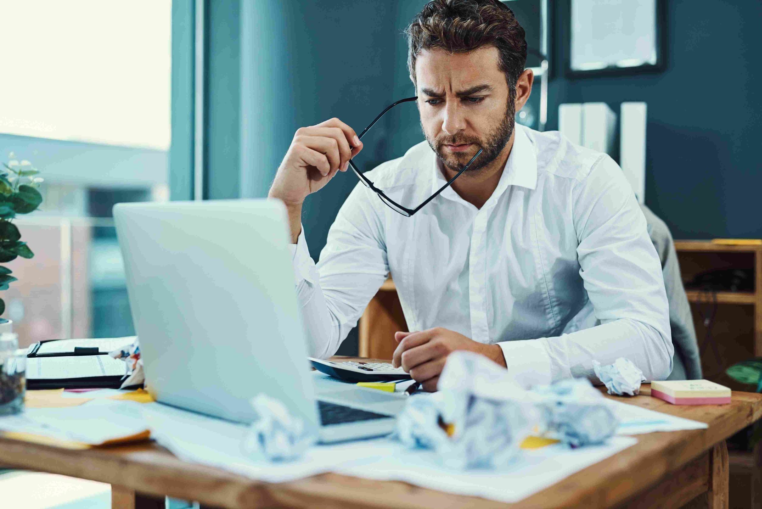 Muškarac sedi za stolom i analizira dokumente uz laptop i kalkulator