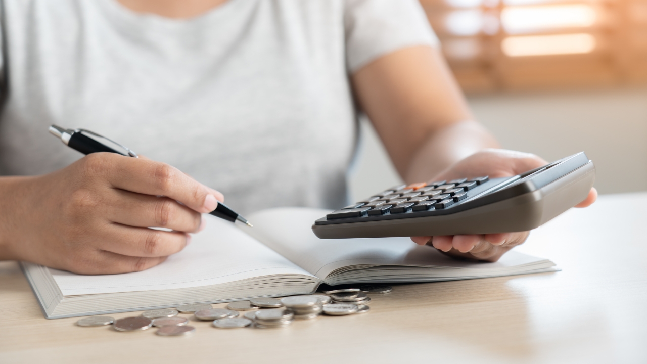 Osoba zapisuje troškove dok računa iznose na kalkulatoru pored novčića